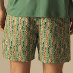 Person wearing green and orange fish patterned swim shorts on a beige background.