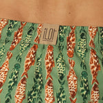 Close up of green and orange fish-patterned swim shorts with a brand label on a beige background.