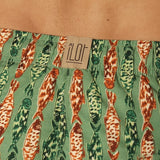 Close up of green and orange fish-patterned swim shorts with a brand label on a beige background.