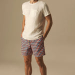 Man wearing a white t-shirt and checkered swim shorts on a beige background.