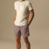 Man wearing a white t-shirt and checkered swim shorts on a beige background.
