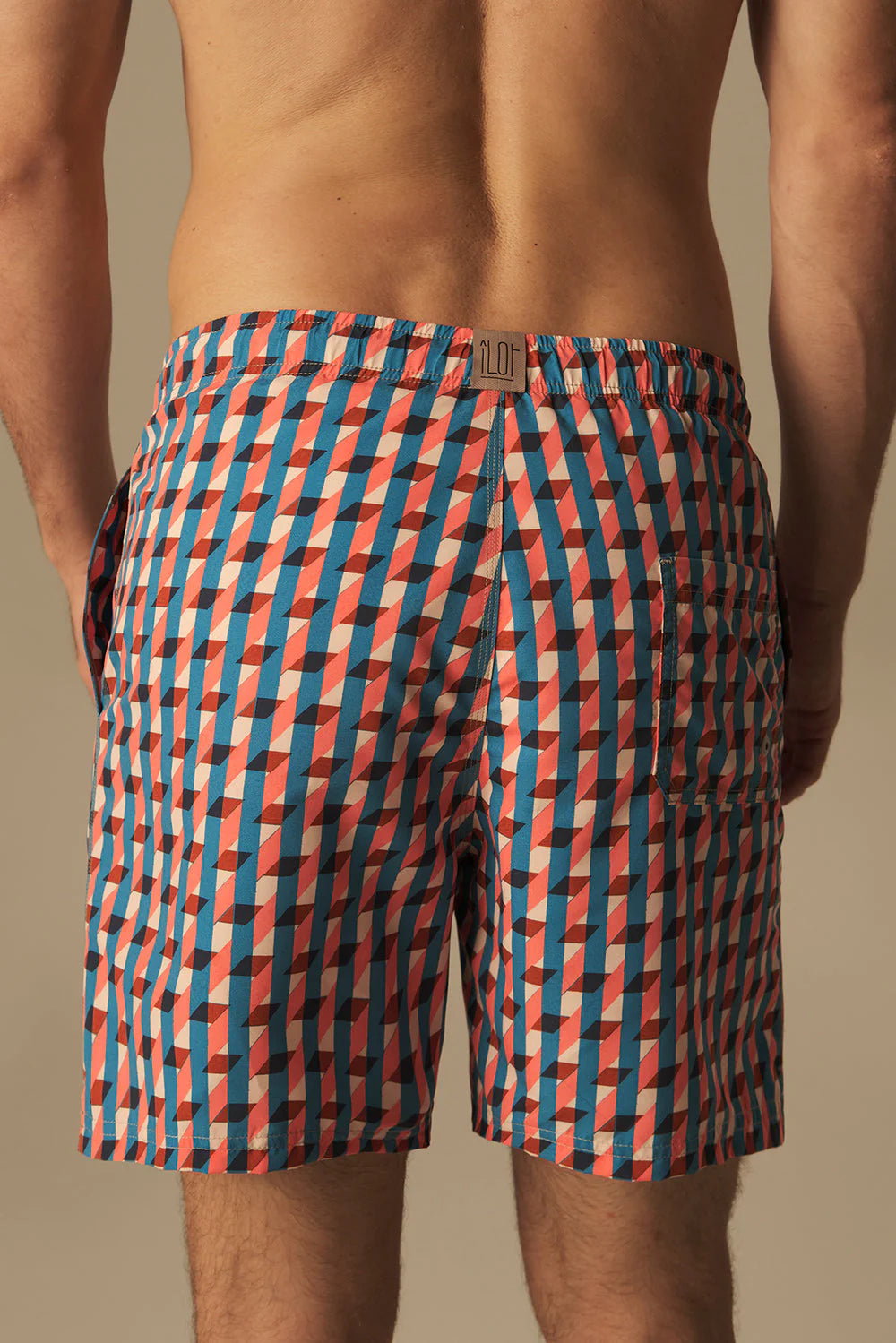 Person wearing a patterned swim shorts on a beige background.