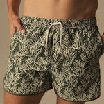 Green and white patterned swim shorts worn by a person on a neutral background.