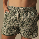 Green and white patterned swim shorts worn by a person on a neutral background.