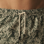 Green swim shorts with a white leaf pattern worn by a person.