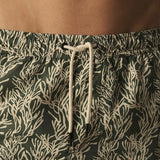 Green swim shorts with a white leaf pattern worn by a person.