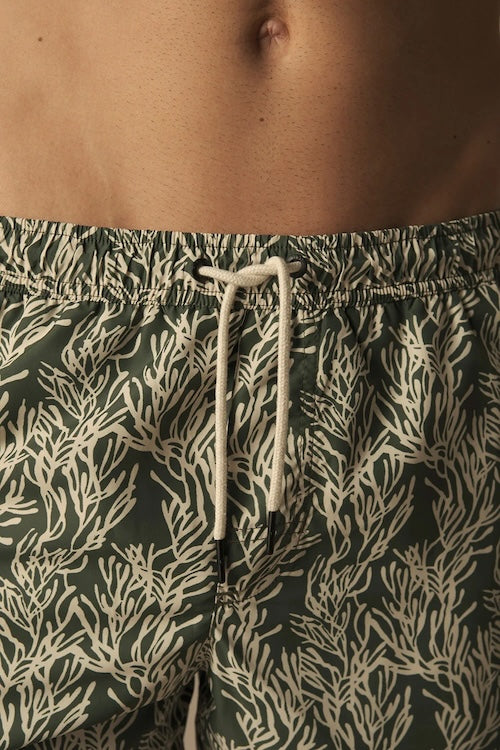 Green swim shorts with a white leaf pattern worn by a person.