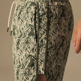 Green and white leaf patterned swim trunks worn by a person on a neutral background.