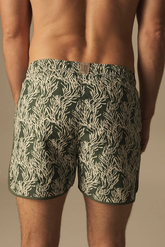 Man wearing green swim trunks neutral leaf pattern. 