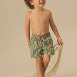 Child wearing green and orange fish patterned shorts standing on a beige background.