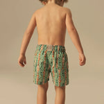 Child wearing green and orange fish patterned swim shorts on a beige background.