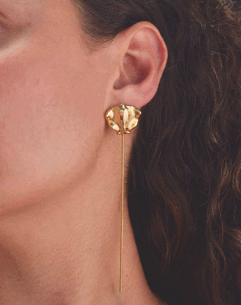 Close-up of gold sting ray earring worn by a person with dark hair.
