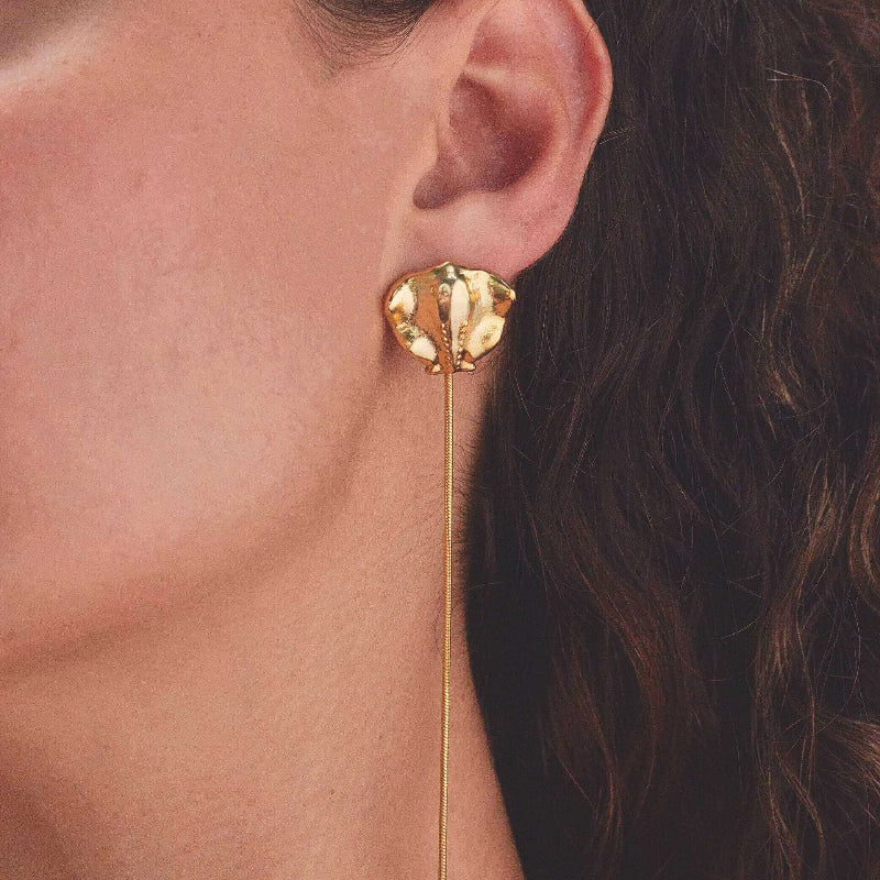 Close-up of gold sting ray earring worn by a person with dark hair.