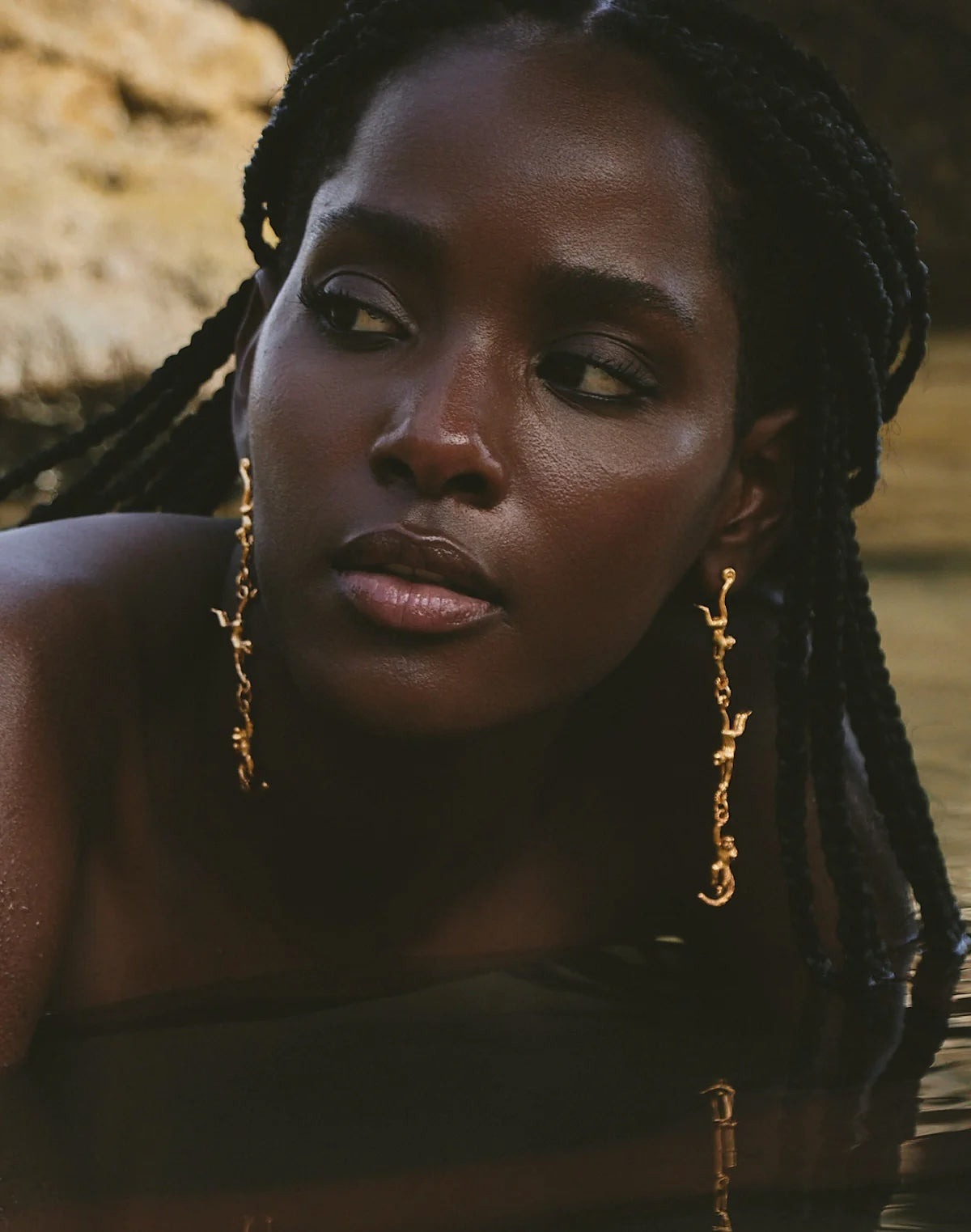 Woman with braided hair wearing gold earrings against a blurred natural background