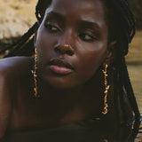 Woman with braided hair wearing gold earrings against a blurred natural background