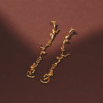 Gold branch-shaped earrings on a brown background