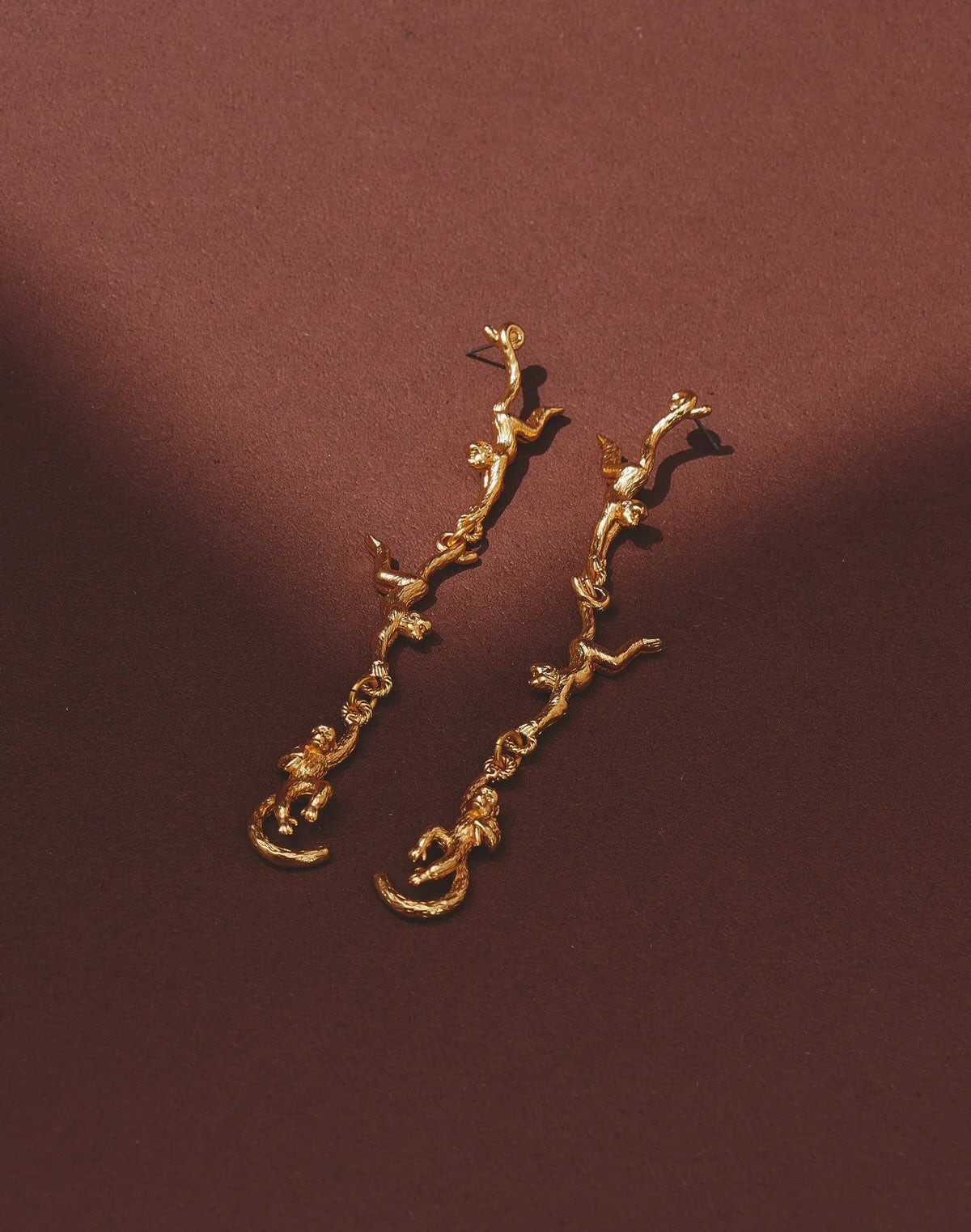 Gold branch-shaped earrings on a brown background