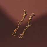 Gold branch-shaped earrings on a brown background