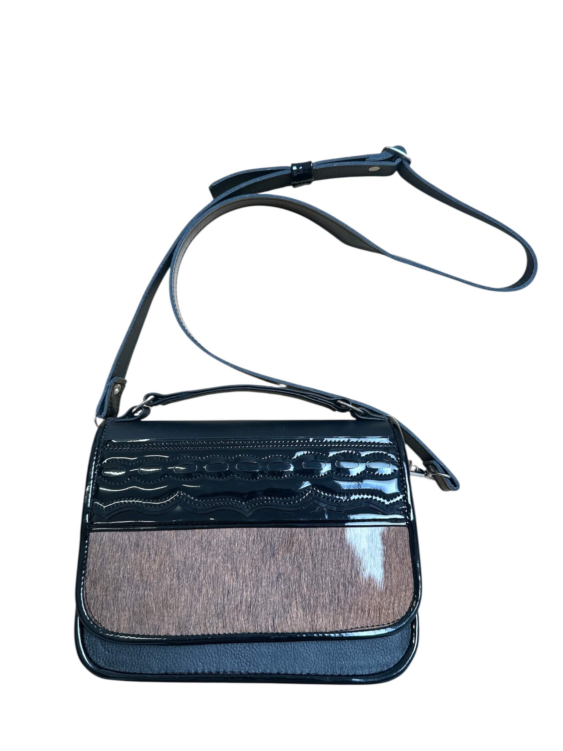 Black carriel crossbody purse with a strap and cow hide material on a white background.