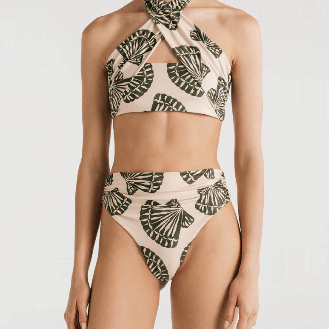 A a bikini with a halter top design and a shell print, featuring a crisscross design at the front and an adjustable tie at the back, with high waisted cheeky bikini bottoms, worn by a model. 