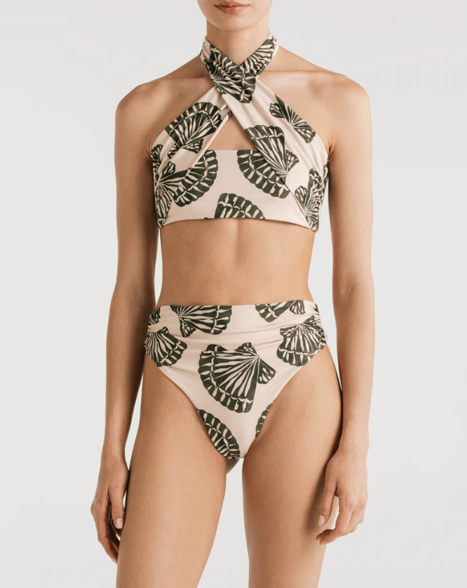 A a bikini with a halter top design and a shell print, featuring a crisscross design at the front and an adjustable tie at the back, with high waisted cheeky bikini bottoms, worn by a model. 