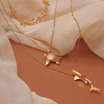 Gold necklaces with starfish, turtle and whale pendants on a beige fabric background.