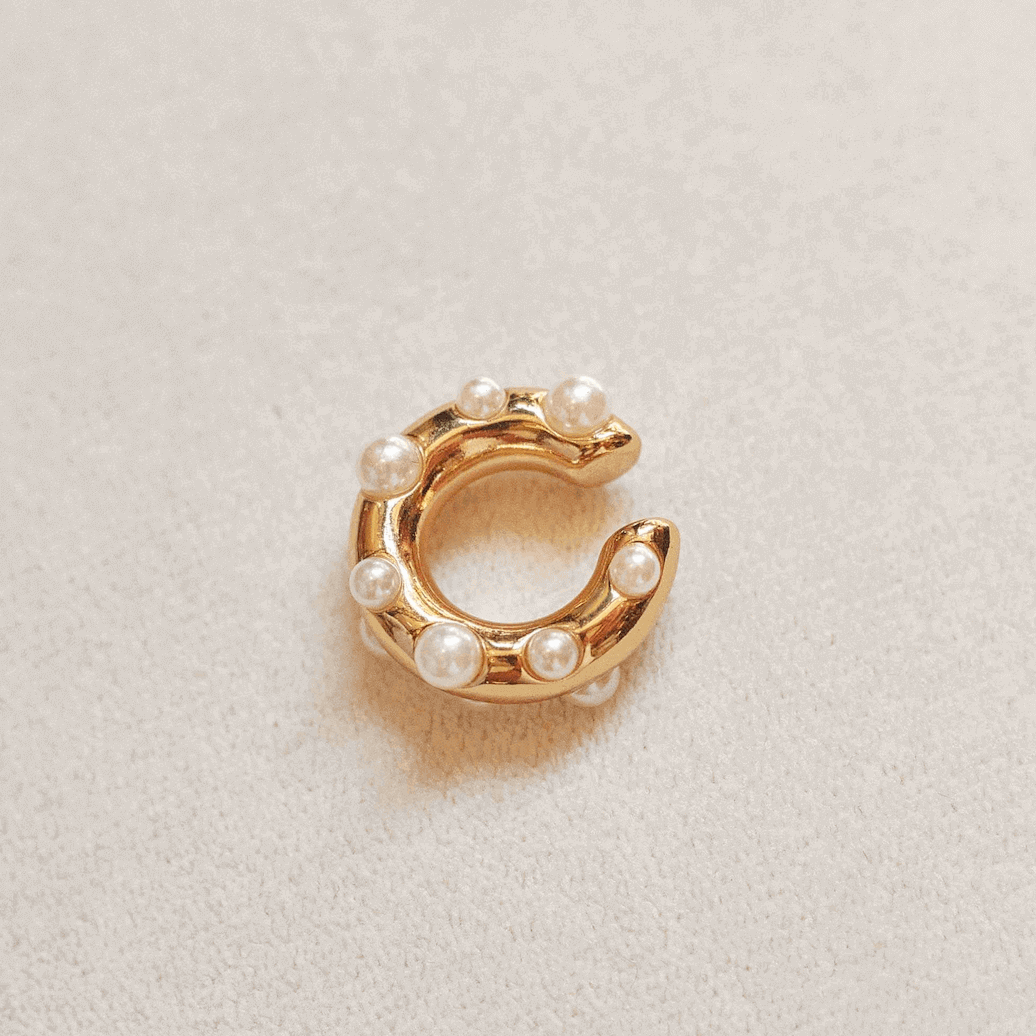Gold ear-cuff with pearl beads on a light beige background.