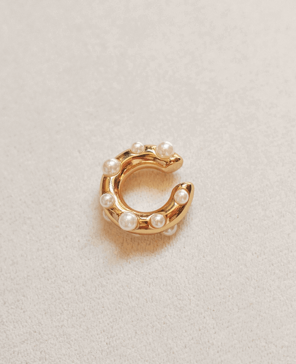 Gold ear-cuff with pearl beads on a light beige background.