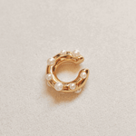 Gold ear-cuff with pearl beads on a light beige background.