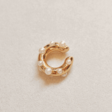 Gold ear-cuff with pearl beads on a light beige background.