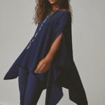 Woman wearing a blue poncho over a dark outfit against a plain background.