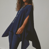 Woman wearing a blue poncho over a dark outfit against a plain background.