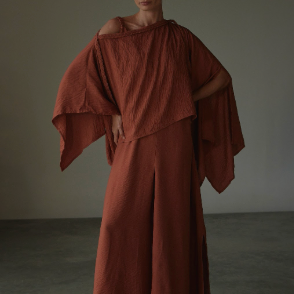 Woman wearing a terracota dress against a plain background.