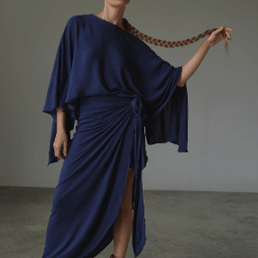 Woman wearing a blue skirt and blouse dress with a plain background.