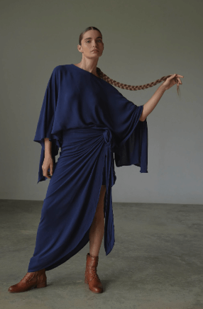 Woman wearing a blue skirt and blouse dress with a plain background.