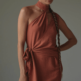 Woman wearing a rust-colored dress against a gray background.