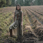 Woman in a long, flowing dress standing in a field with trees in the background