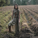 Woman in a long, flowing dress standing in a field with trees in the background