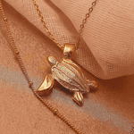 Gold turtle pendant necklace on a soft fabric background.