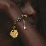 Gold bracelet with a circular charm and jade beads worn by a model.
