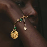 Gold bracelet with a circular charm and jade beads worn by a model.