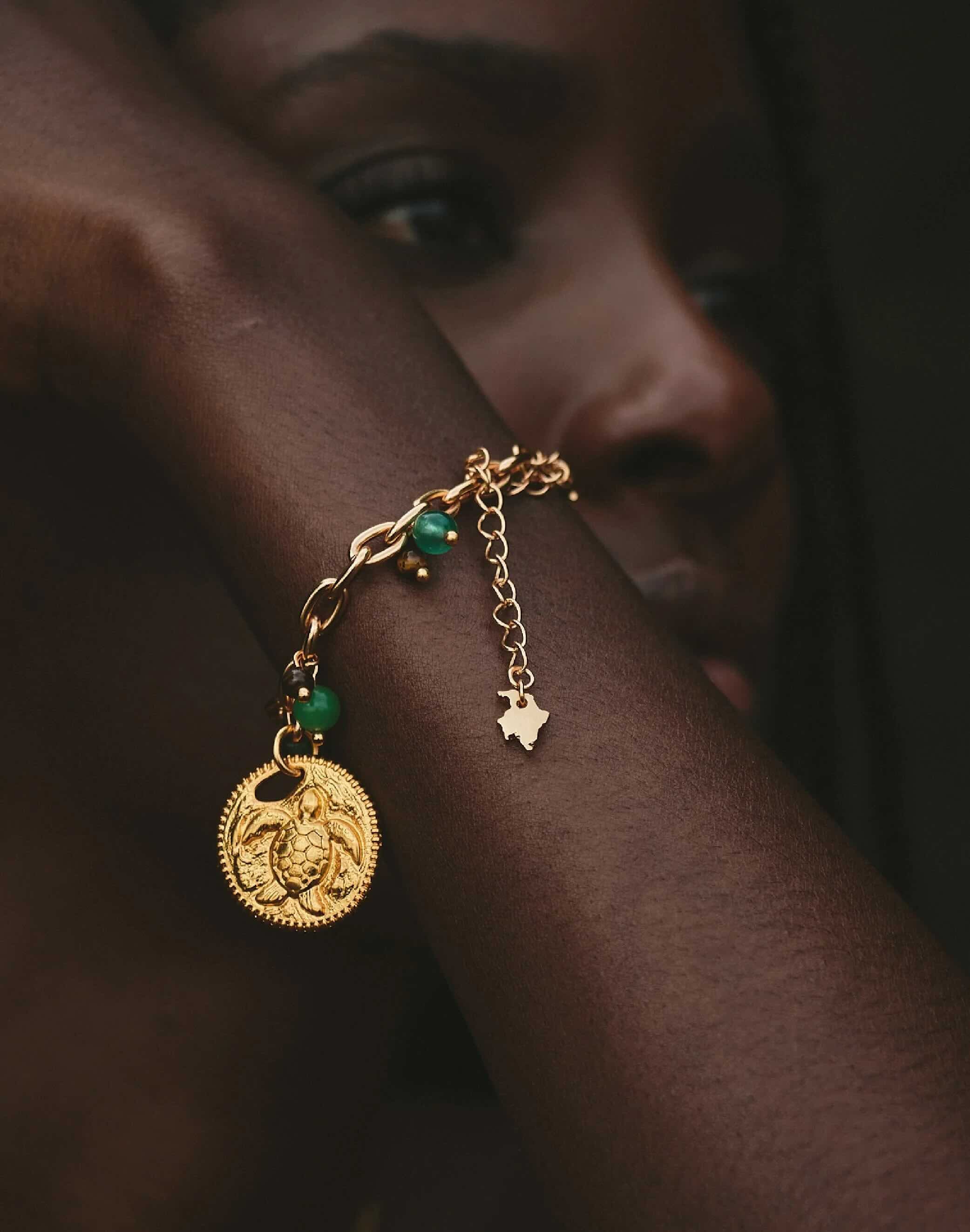 Gold bracelet with a circular charm and jade beads worn by a model.