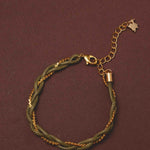 Bracelet with green braided design and gold chain on a brown background