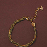 Bracelet with green braided design and gold chain on a brown background