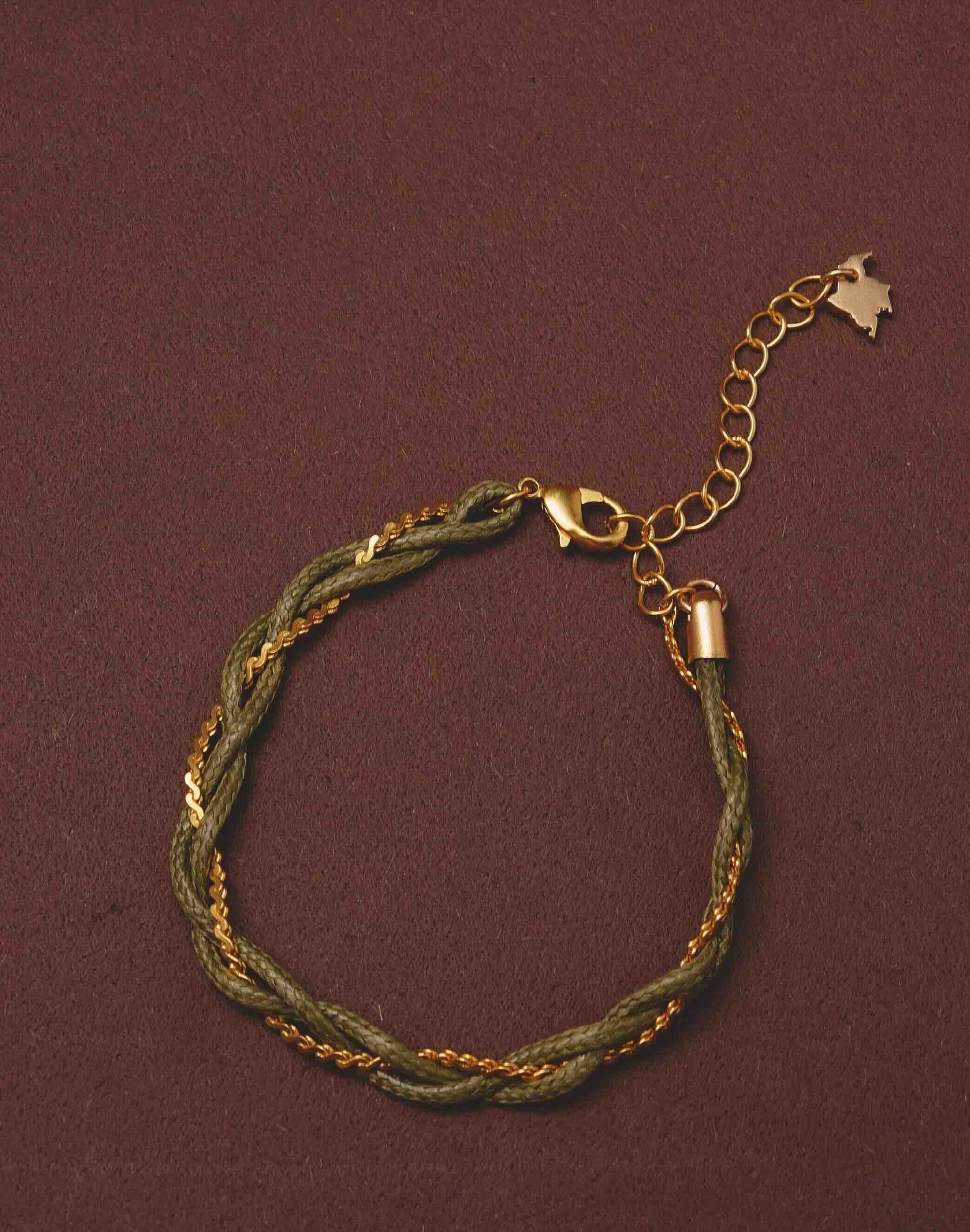 Bracelet with green braided design and gold chain on a brown background