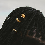Black knitted box braids with gold turtle brooches on a light gray background