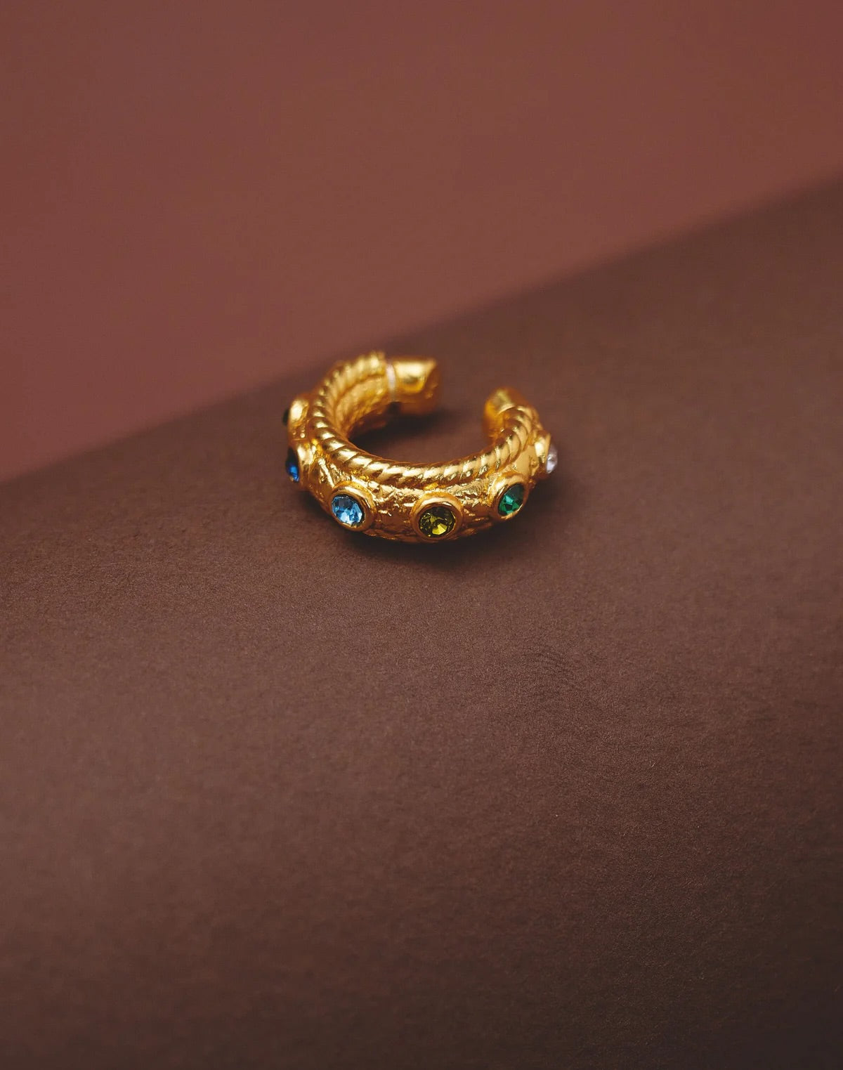 Gold hoop earring with gemstones on a brown background