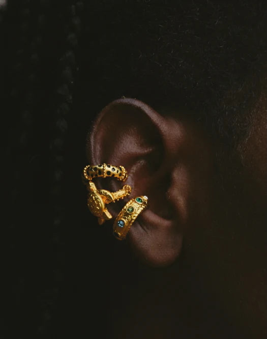Gold earring with green gemstones on a dark background