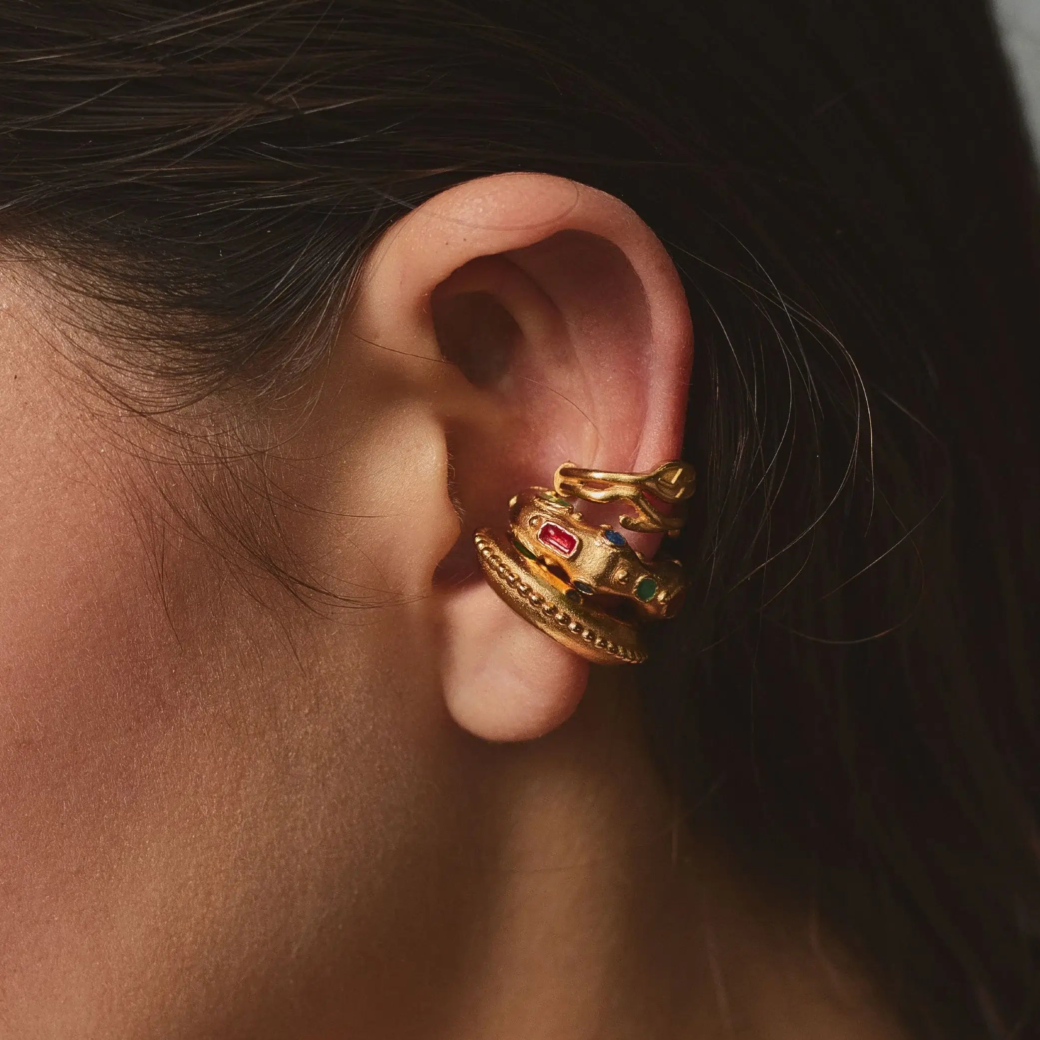 Close-up of a gold ear cuff stack with gemstones worn by a person.