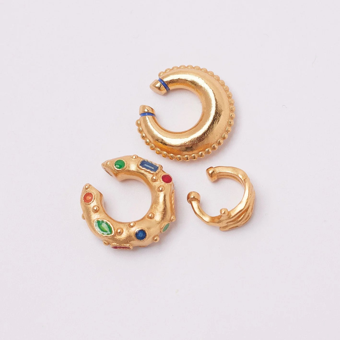 Gold hoop earrings with colorful gemstones on a light gray background.